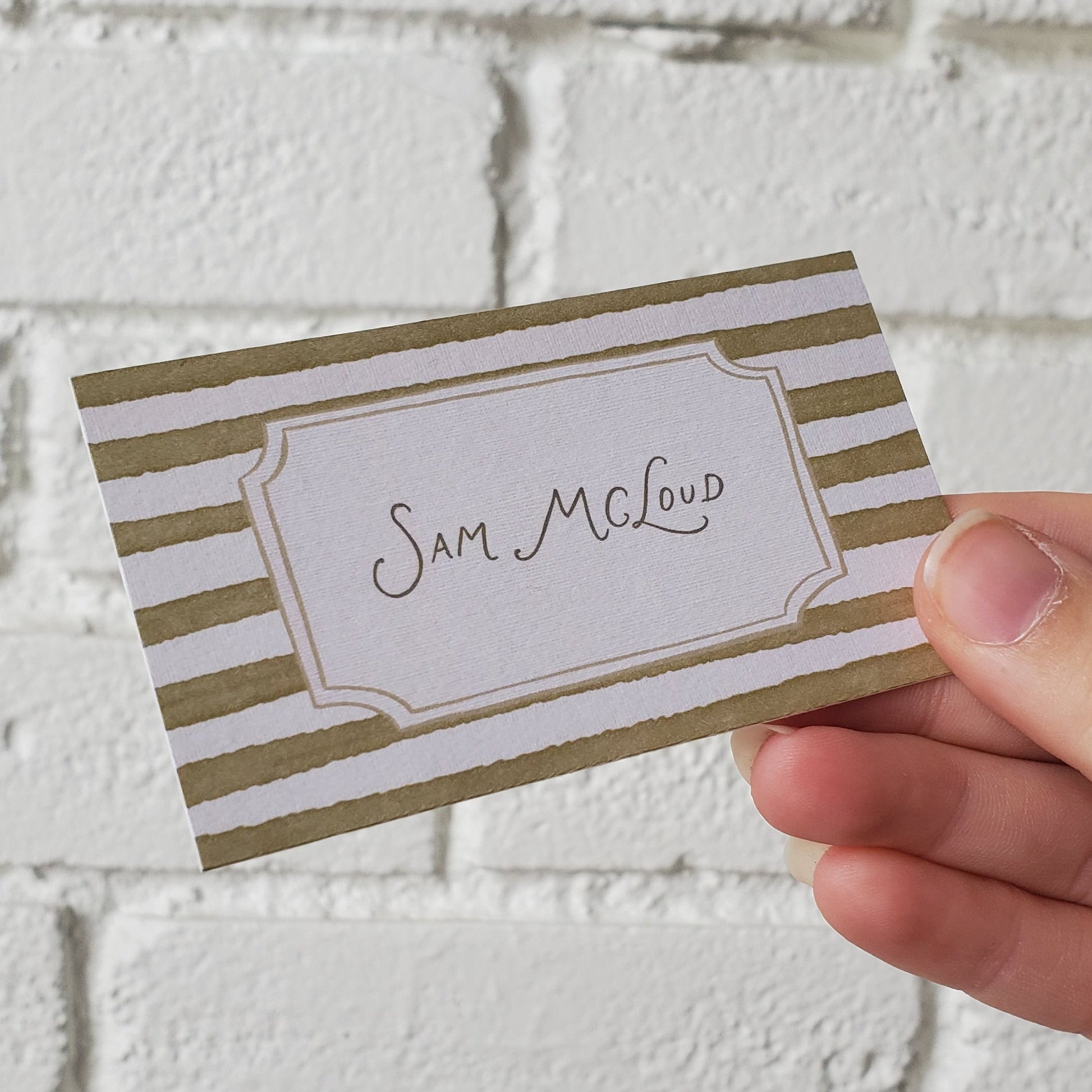 Hand holding a striped name tag against a textured white background