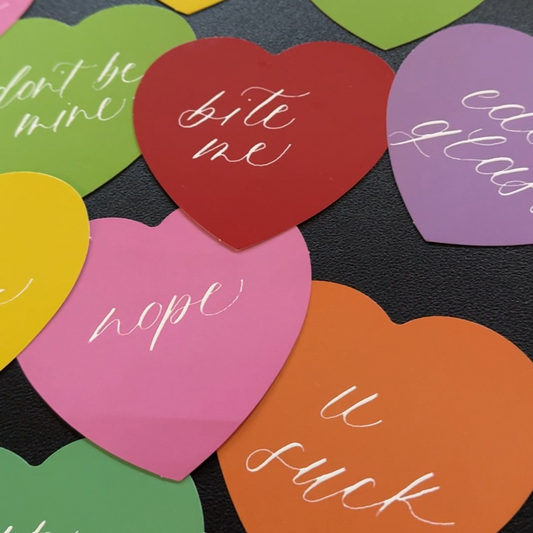 Colorful heart-shaped stickers with various phrases on a black background