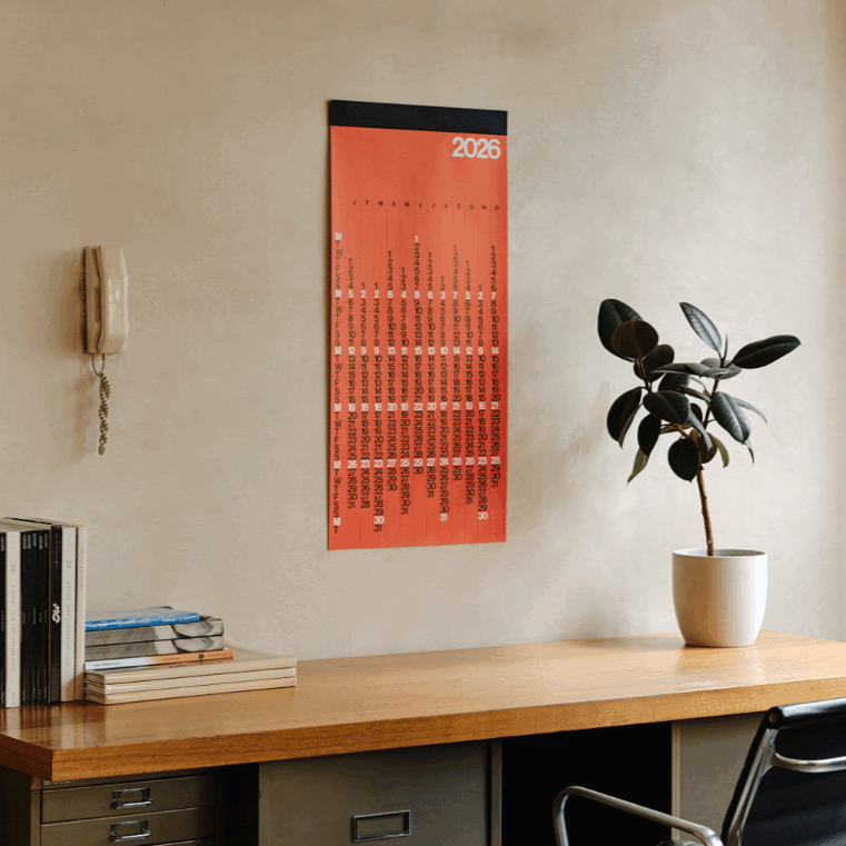 Calendar on a wall above a desk with a plant and office supplies.