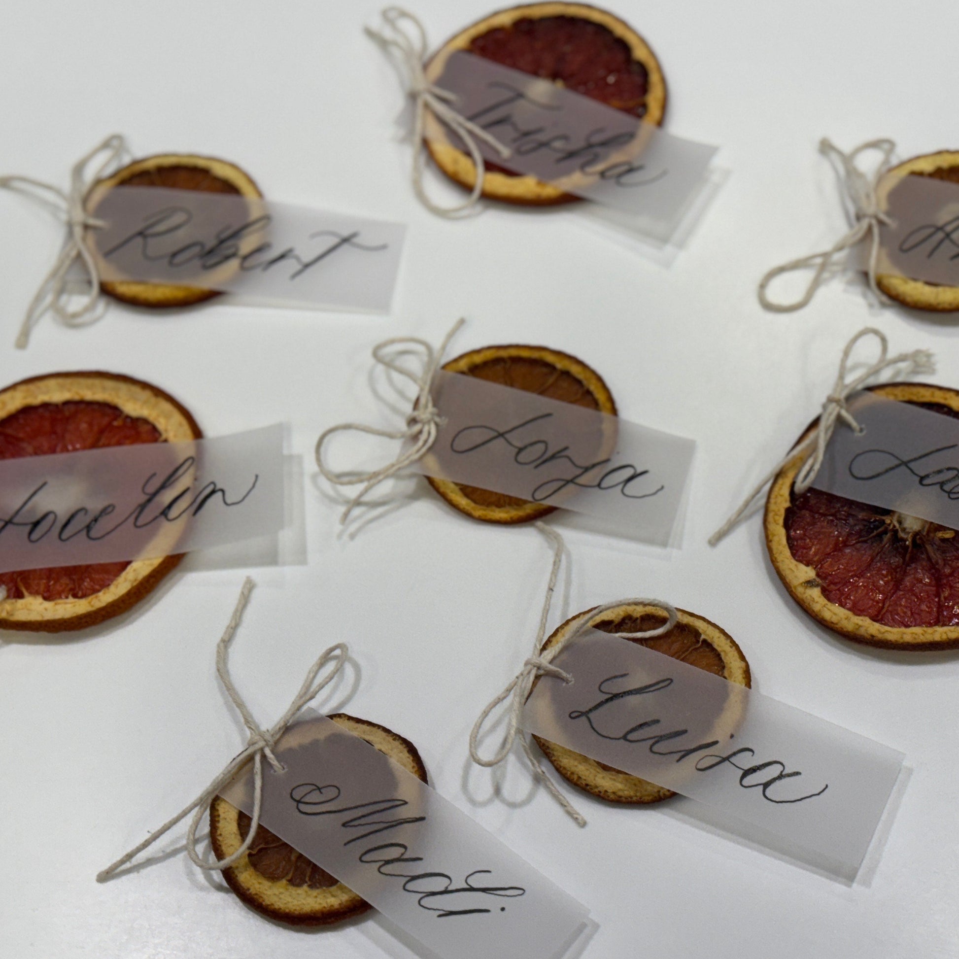 Decorative name tags attached to dried orange slices on a white surface